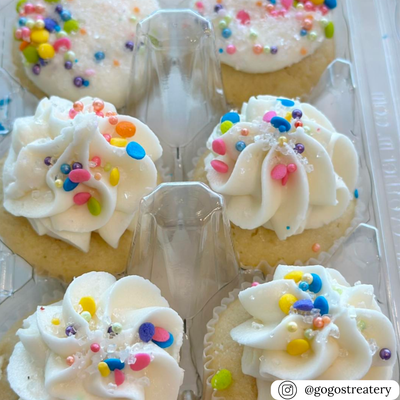 Cupcakes with white frosting and colorful sprinkles in a clear plastic egg carton container.