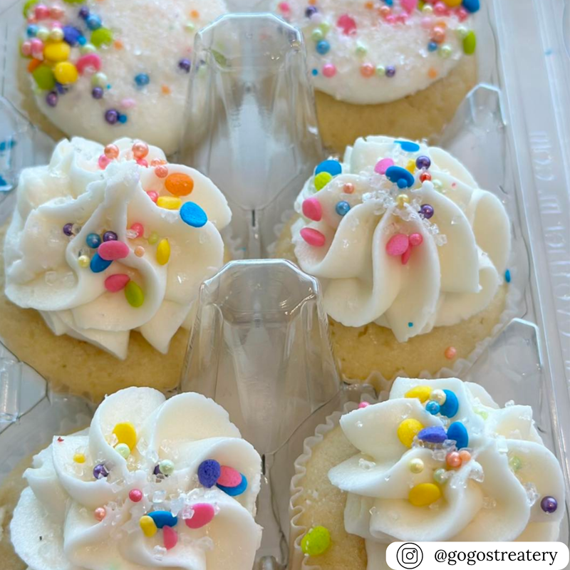 Cupcakes with white frosting and colorful sprinkles in a clear plastic egg carton container.