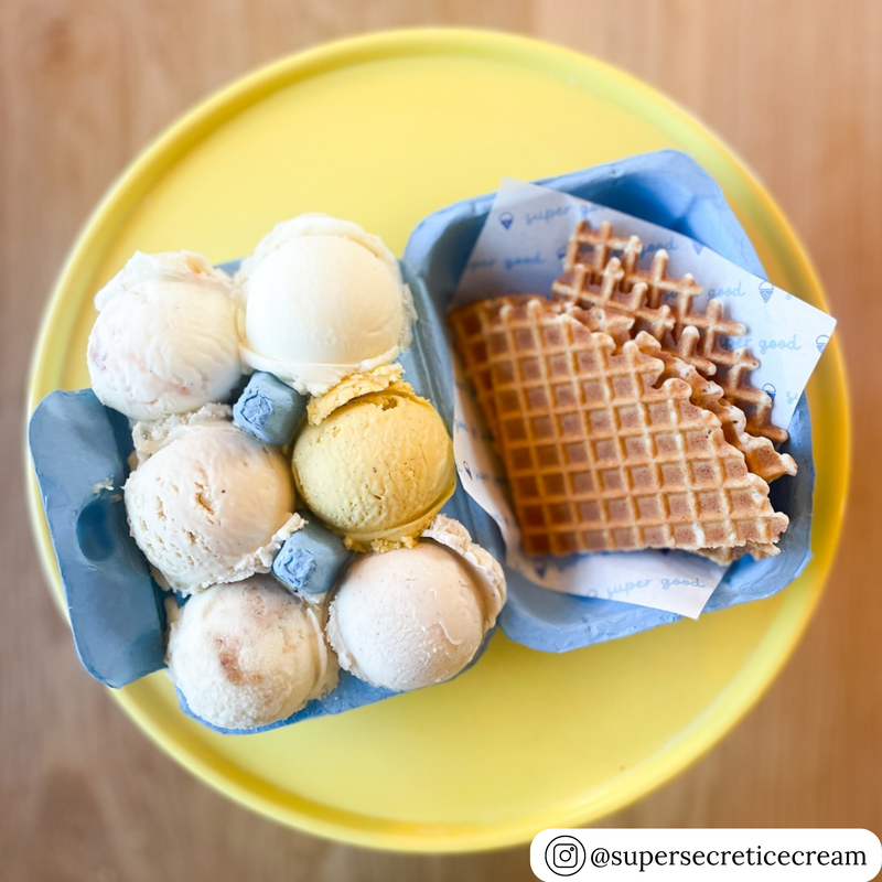 Ice cream flight in an egg carton with waffle cones on a yellow plate